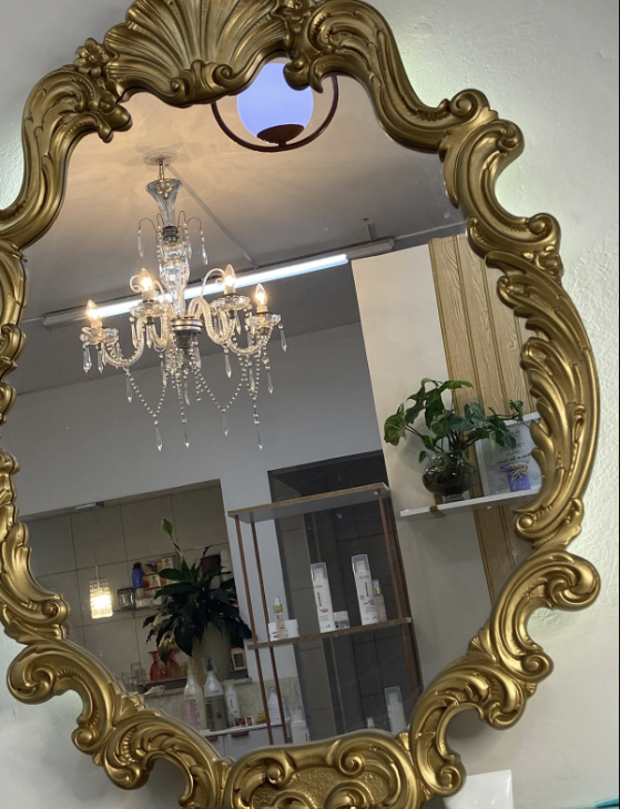 Espelho dourado do Studio Michele Copertino refletindo o lustre e o espaço de atendimento